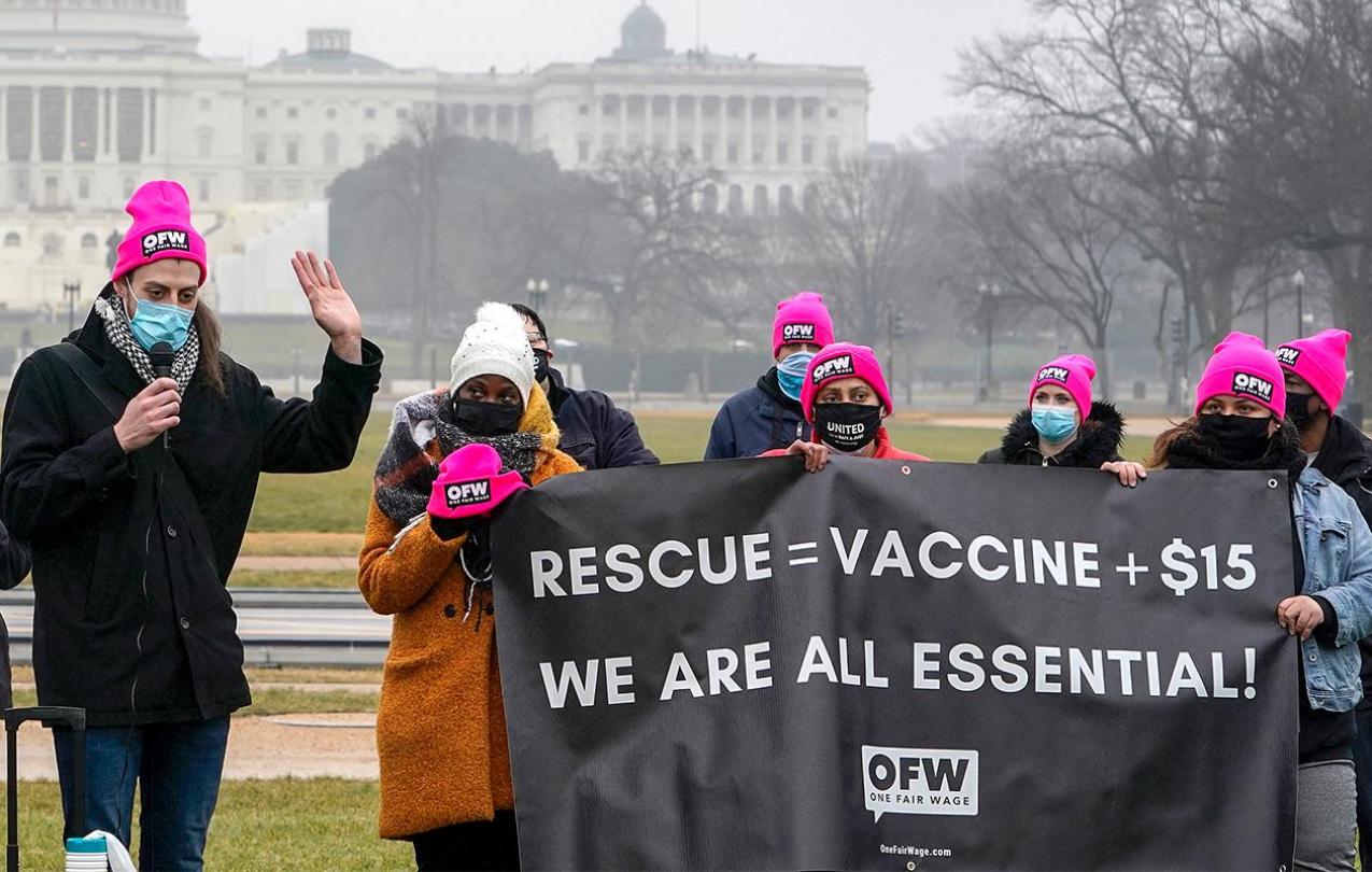 Protestors holding banner that says "RESCUE = VACCINE + $15", next line "WE ARE ALL ESSENTIAL"