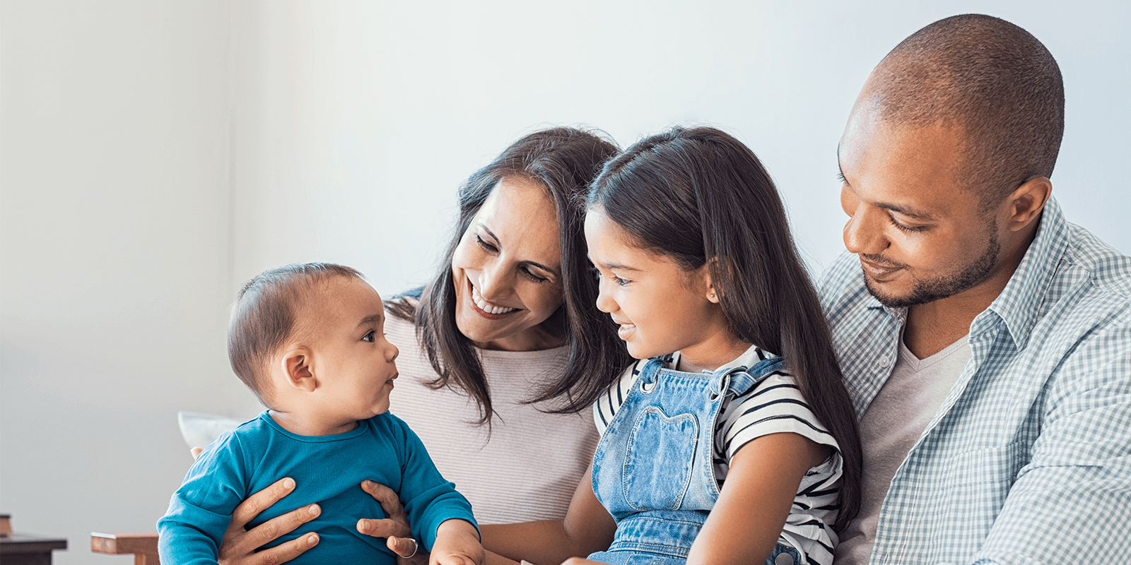 Photograph of family of four sitting together and looking at each other contentedly. 